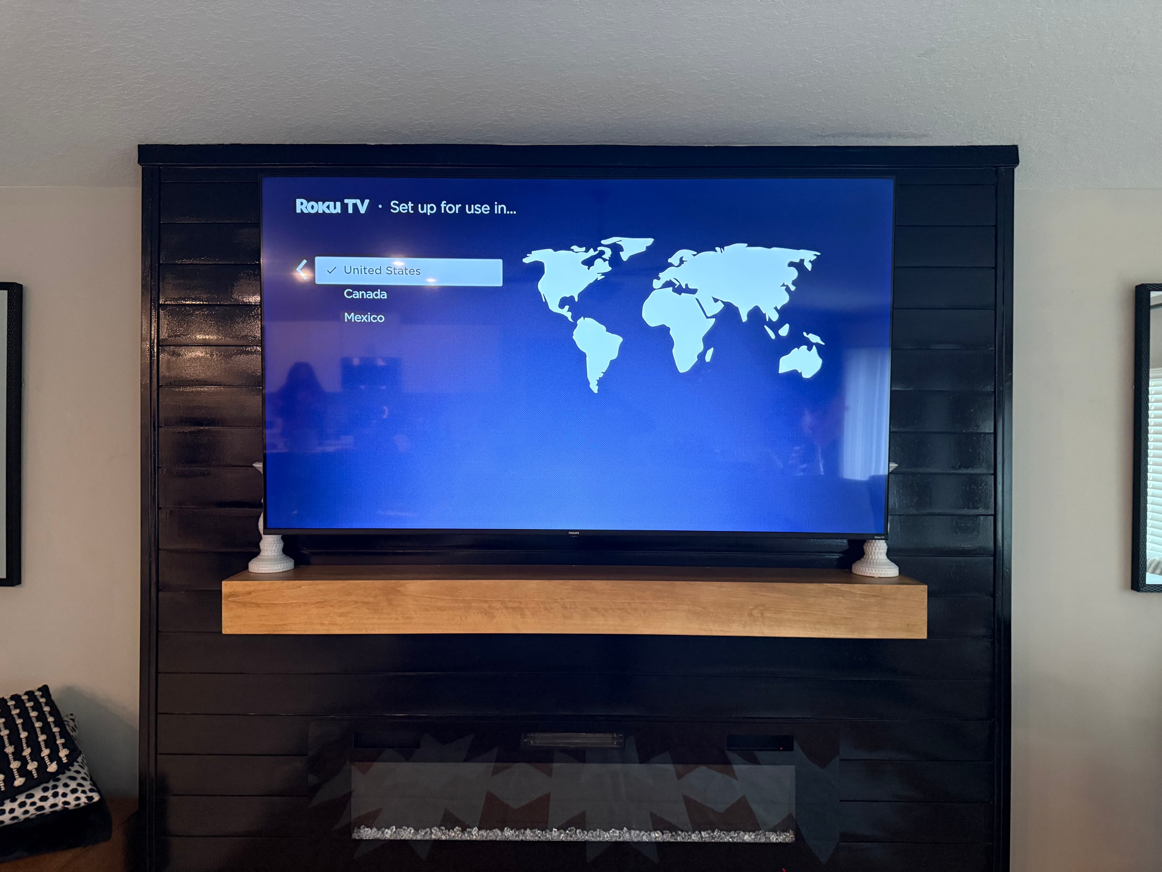 TV mounted over fireplace with floating wood mantle on black shiplap wall, Tampa